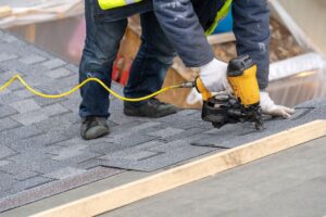 roof patch worker using nailgun to apply shingles