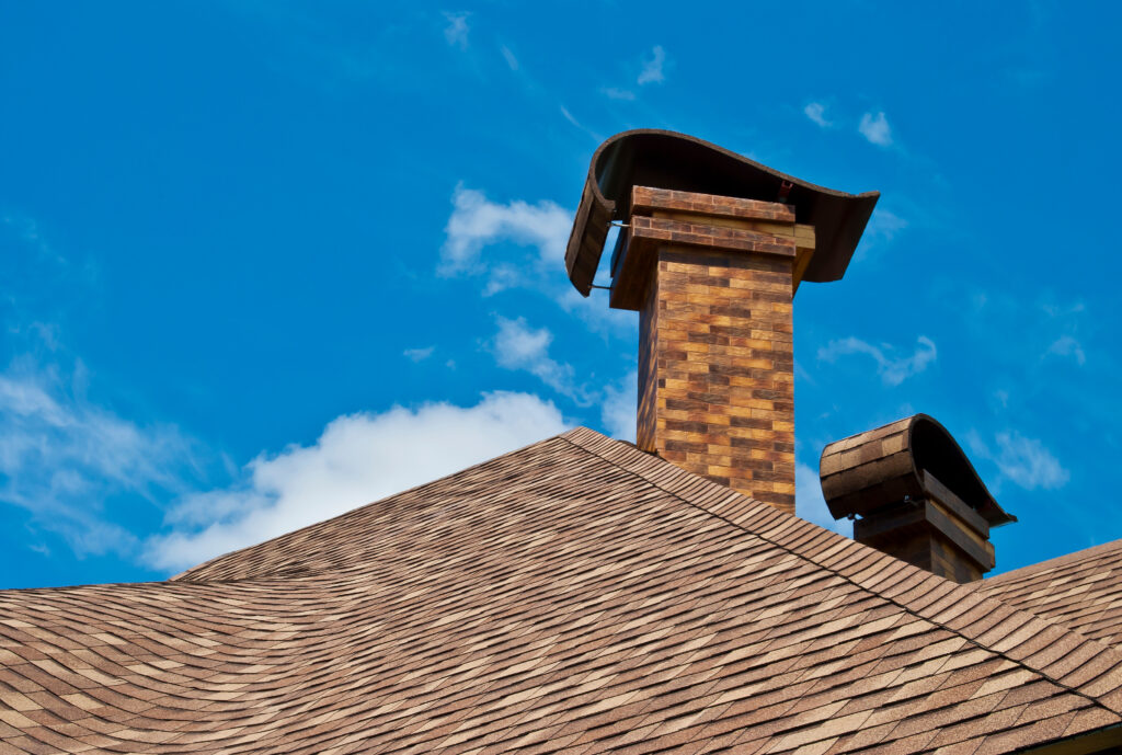 The roof of the house with two chimneys in the new design against the blue sky with clouds.
